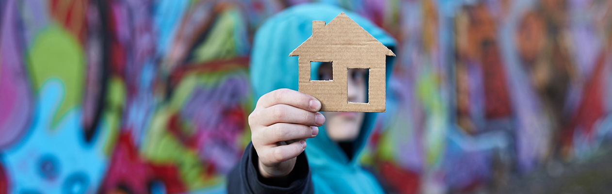 homeless boy holding cutout house in hand